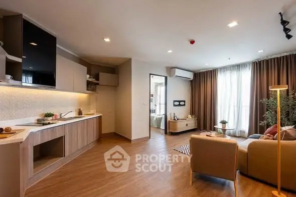 Modern living room with open kitchen and cozy seating area, featuring stylish decor and ample natural light.