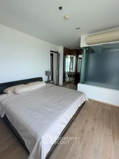Spacious bedroom with modern design and wooden flooring, featuring a large bed and air conditioning.