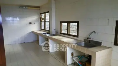 Spacious kitchen with dual sinks and tiled countertops in a sunlit room.