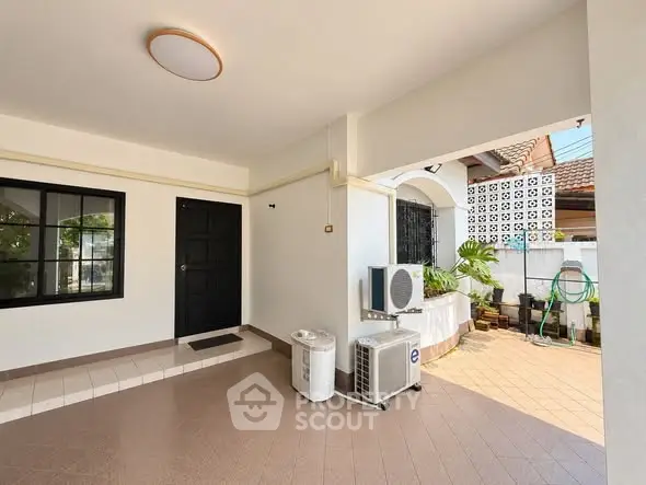 Spacious covered outdoor area with modern air conditioning unit and stylish black door.