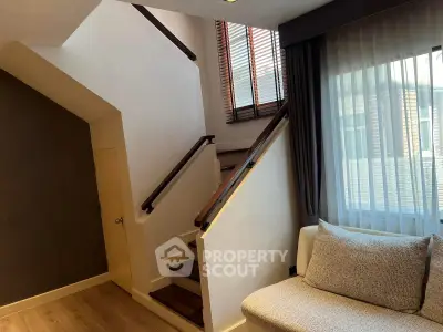 Charming living room with staircase and cozy seating area, featuring natural light and modern design.