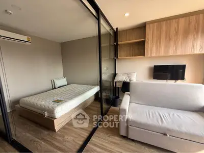 Modern studio apartment with glass partition, cozy bed, and stylish sofa in a well-lit space.