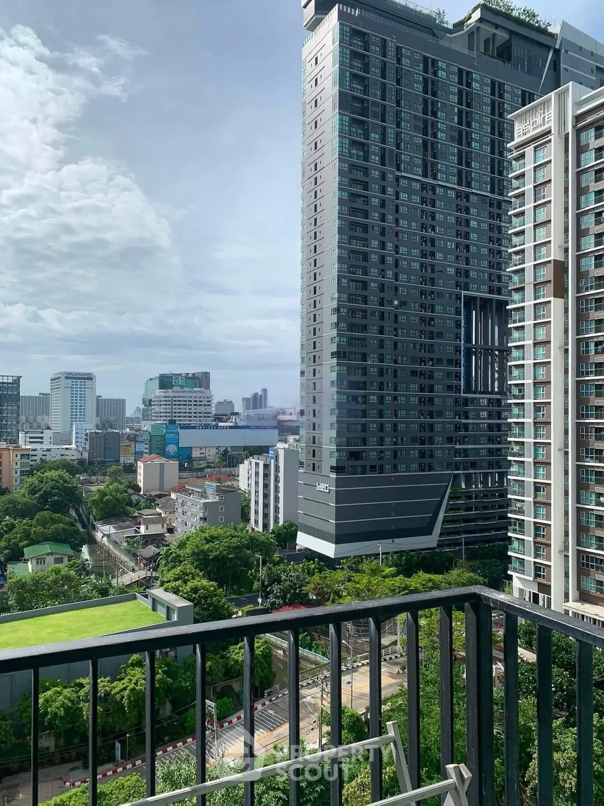 Stunning cityscape view from a high-rise balcony overlooking modern urban architecture and lush greenery.
