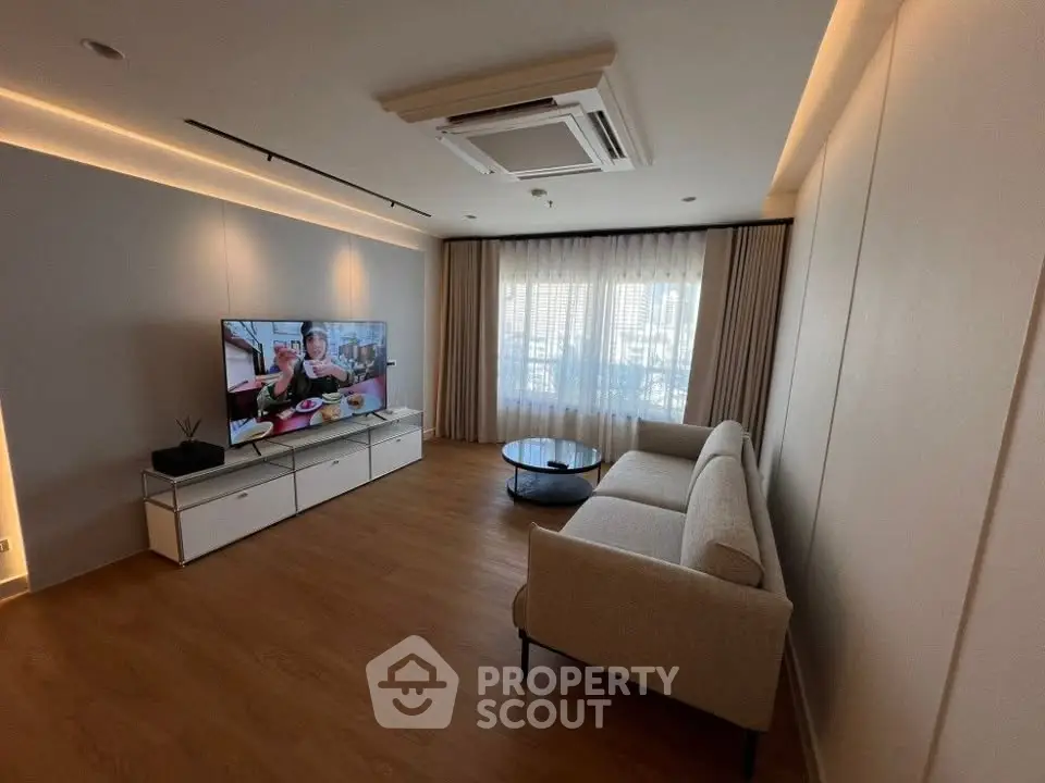 Spacious modern living room with elegant sofa and large TV, featuring natural light from large windows.