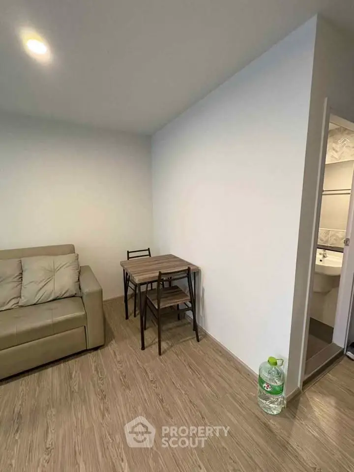 Cozy living room with wooden flooring, compact dining set, and a glimpse of a modern bathroom.
