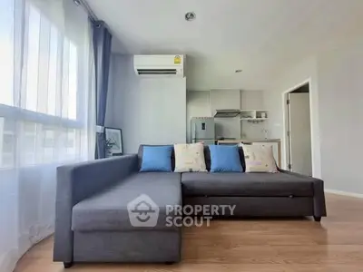 Modern living room with sleek gray sofa and open kitchen layout in bright apartment.