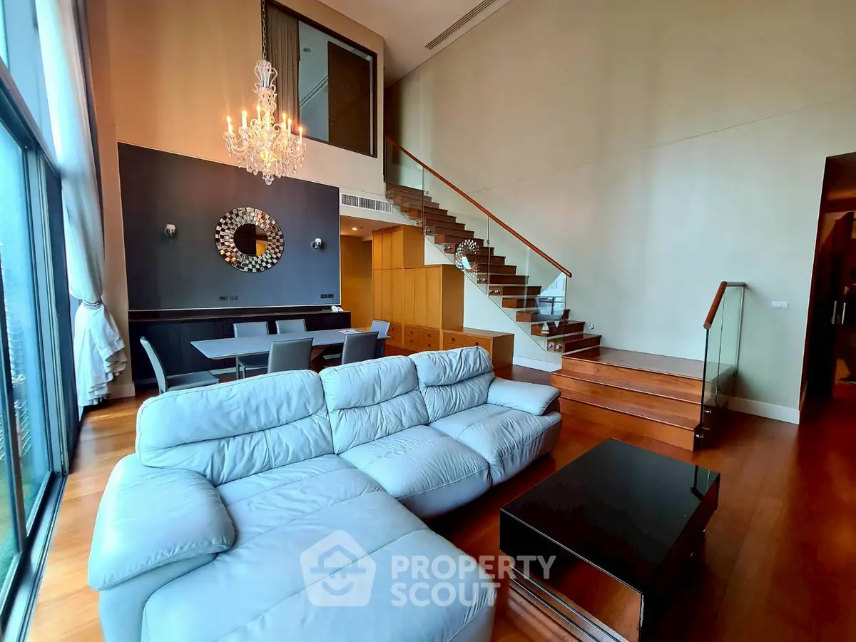 Luxurious living room with high ceiling, elegant chandelier, and modern staircase in a stylish apartment.