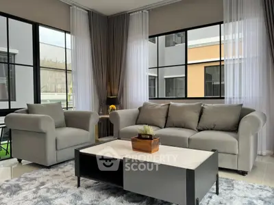 Modern living room with stylish gray sofa and armchair, large windows, and elegant decor.