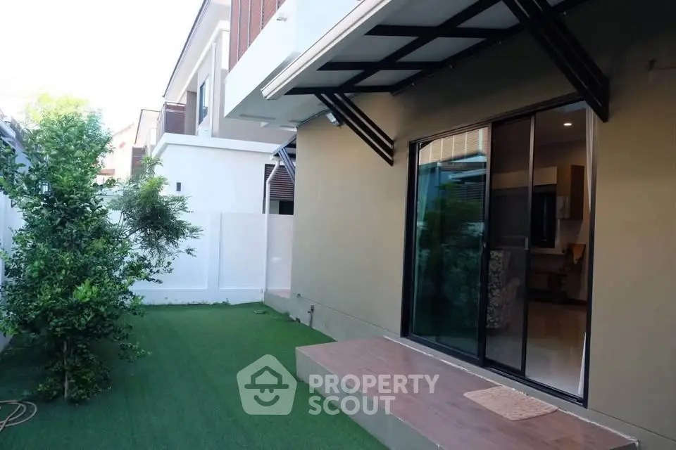 Modern home exterior with sliding glass doors and artificial grass lawn.