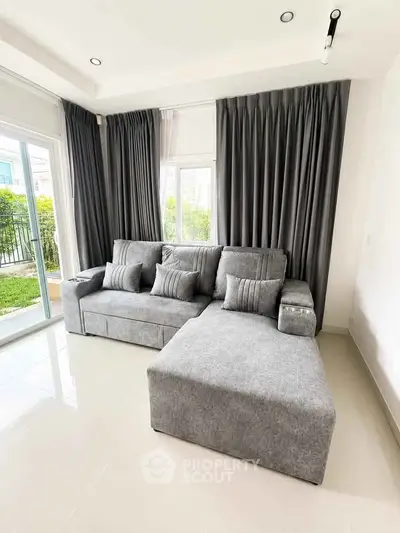 Modern living room with stylish gray sofa and large windows overlooking garden