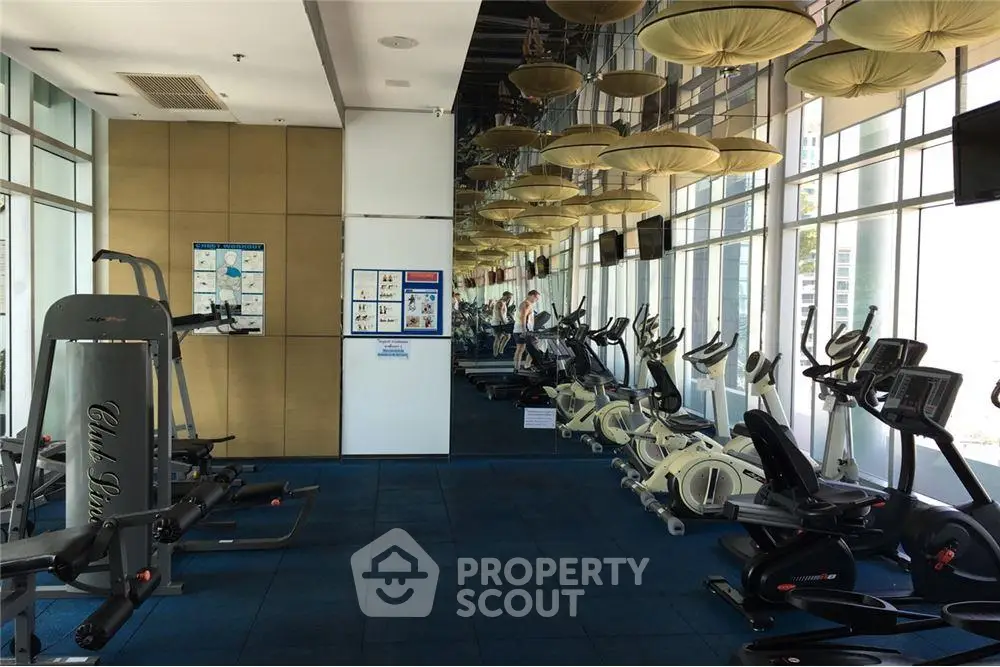 Spacious gym with modern equipment and large windows offering city views.