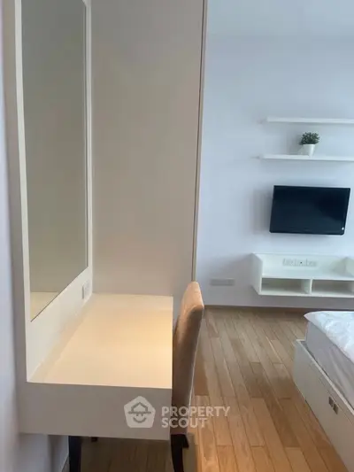 Modern bedroom with sleek furniture and wall-mounted TV, featuring a minimalist design and wooden flooring.