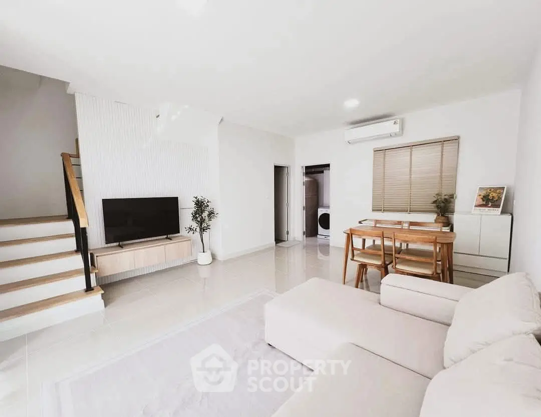 Modern living room with staircase, TV, and dining area in bright, minimalist design.