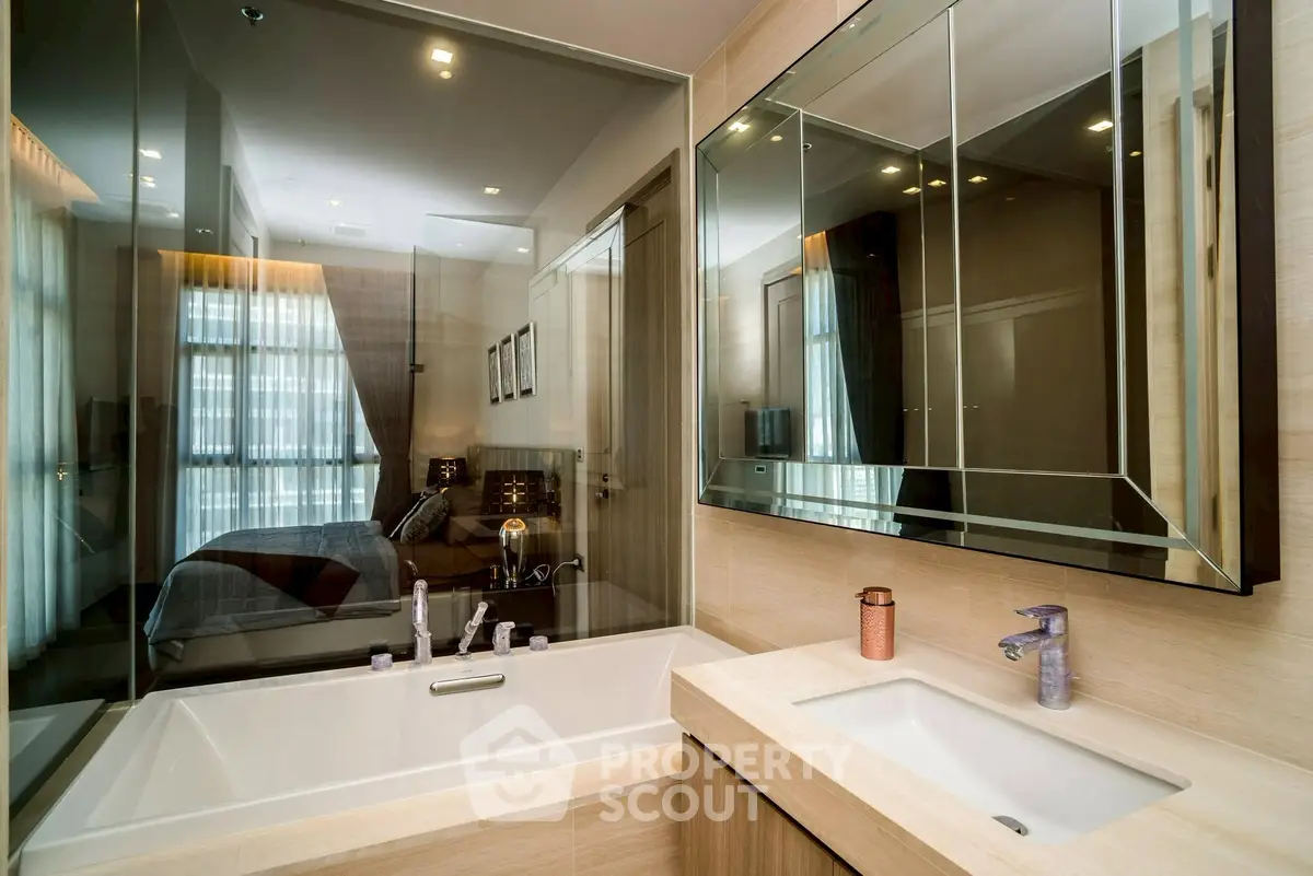 Modern bathroom with elegant fixtures and a glass partition overlooking a bedroom, featuring a sleek bathtub and stylish sink.