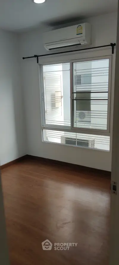 Bright empty room with wooden flooring and large window, perfect for a cozy bedroom setup.