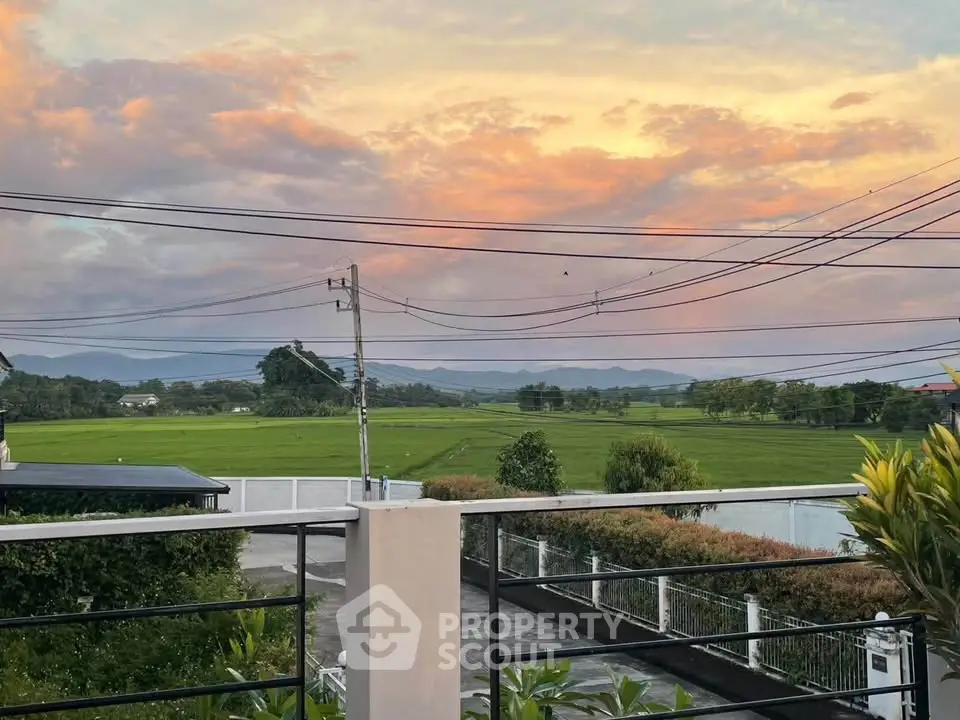 Stunning sunset view from a balcony overlooking lush green fields and distant mountains.