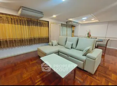 Spacious living room with elegant sofa and dining area, featuring hardwood floors and stylish decor.