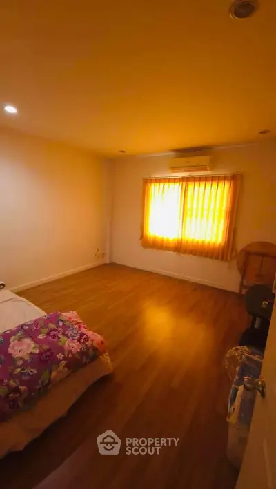 Cozy bedroom with warm lighting and wooden flooring, featuring a bed and air conditioning.