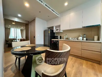 Modern kitchen with dining area, featuring sleek cabinetry and wooden flooring.