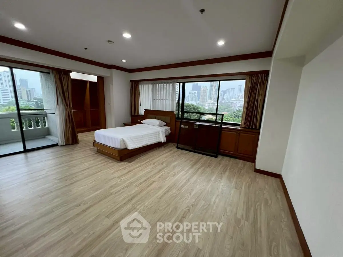 Spacious bedroom with city view and balcony access, featuring wooden flooring and elegant design.