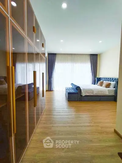 Spacious bedroom with elegant bed and large wardrobe, featuring floor-to-ceiling windows and wooden flooring.
