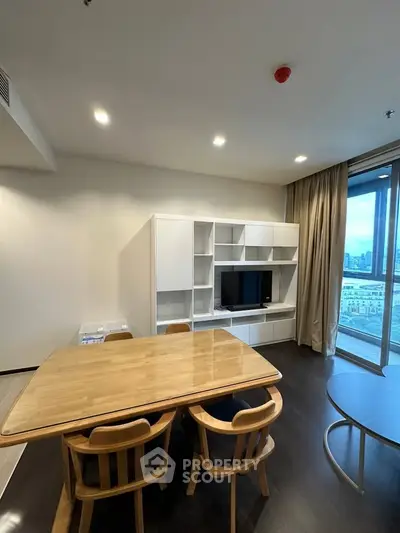 Modern living room with dining area and city view, featuring sleek furniture and large windows.