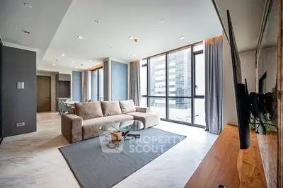 Spacious modern living room with large windows and city view, featuring a cozy sofa and sleek decor.