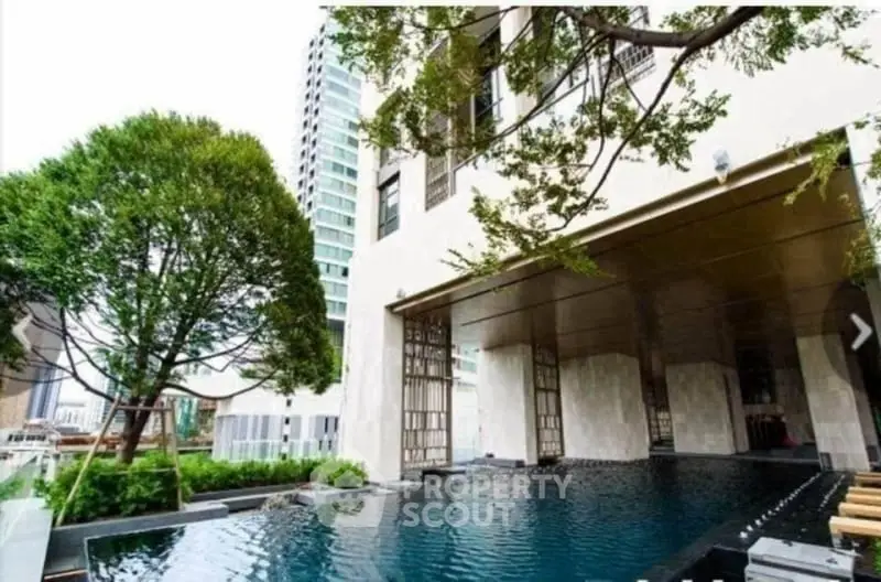 Luxurious modern building with serene pool and lush greenery in urban setting.