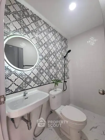 Modern bathroom with stylish tile design and round mirror, featuring a sleek toilet and sink.