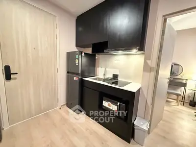 Modern compact kitchen with sleek black cabinets and built-in appliances in a cozy apartment.