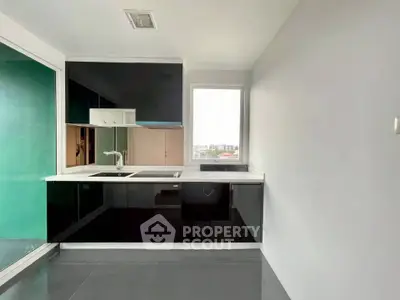 Modern kitchen with sleek black cabinets and large window offering city views.