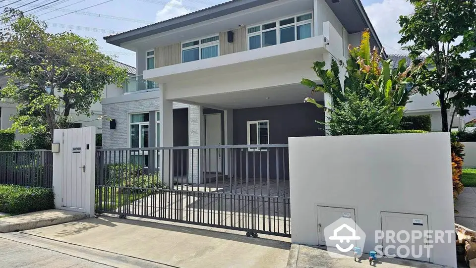 Modern two-story house with gated entrance and lush greenery