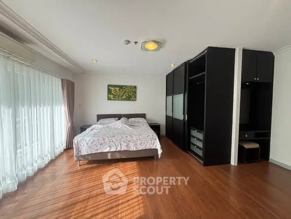 Spacious bedroom with wooden flooring and large window for natural light.