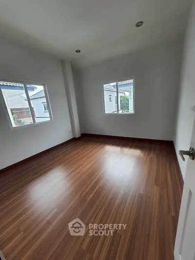 Spacious empty room with wooden flooring and natural light from windows.
