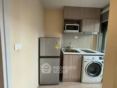 Compact kitchen with fridge, washing machine, and microwave in modern apartment.