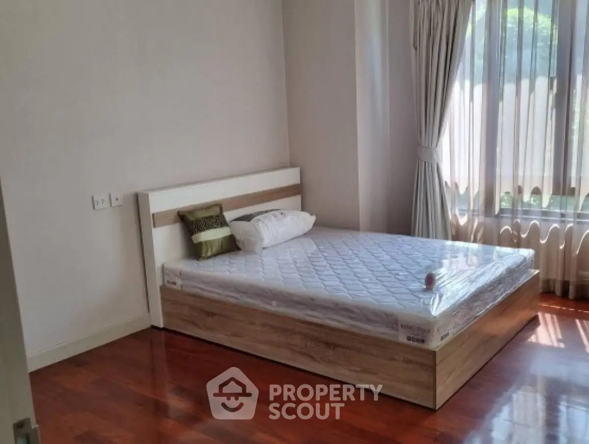 Bright bedroom with wooden flooring and large window, featuring a comfortable bed.
