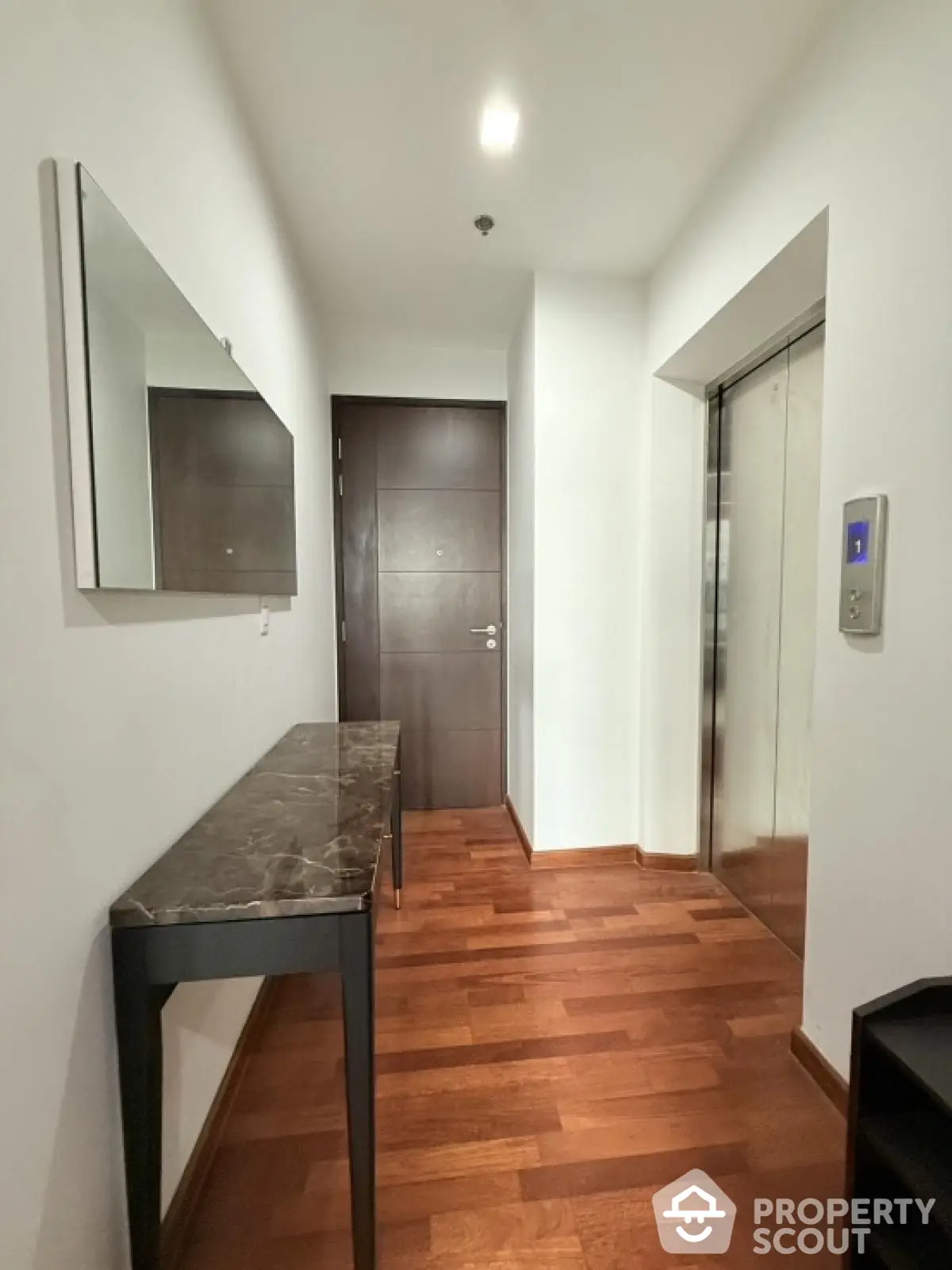 Modern apartment hallway with elegant wooden flooring and sleek elevator access.