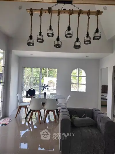 Modern living room with stylish lighting and dining area, featuring large windows and contemporary furniture.