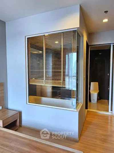 Modern apartment interior with wooden flooring and unique bathroom window feature.