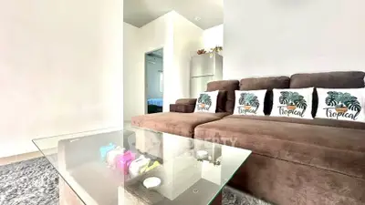 Spacious living room with modern brown sofa and glass coffee table in tropical-themed decor.