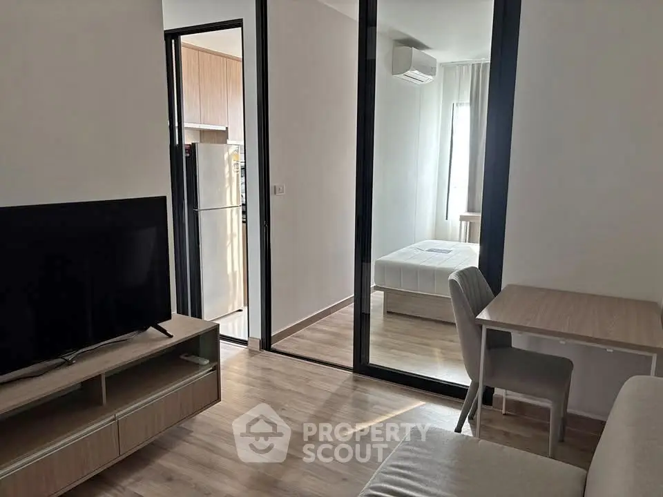 Modern apartment interior with open living area and bedroom, featuring sleek furniture and natural light.