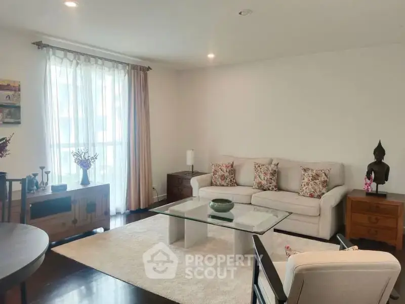 Elegant living room with cozy sofa, glass coffee table, and natural light from large window.