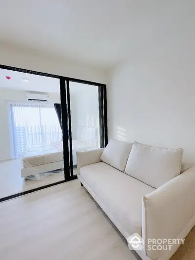 Modern apartment with cozy living room and bedroom separated by glass partition, bright and airy space.