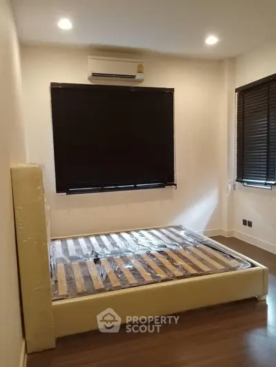 Modern bedroom with new bed frame and air conditioning, featuring sleek blinds and wooden flooring.