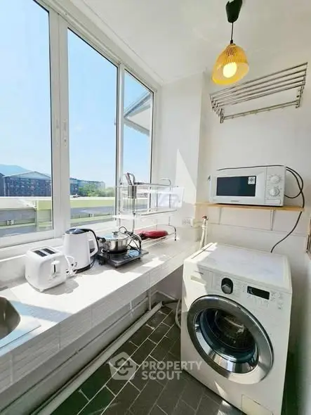 Bright kitchen with modern appliances and washing machine, featuring large windows and ample natural light.