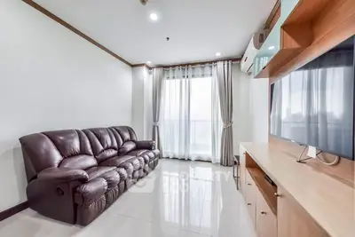 Spacious living room with leather sofa and large TV, featuring modern decor and natural light.