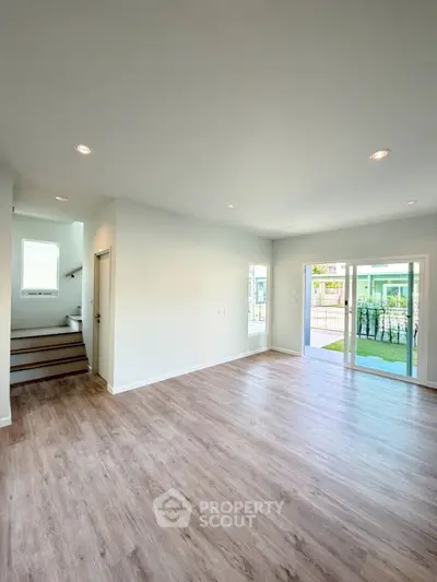 Spacious modern living room with wooden flooring and large windows opening to a garden view.