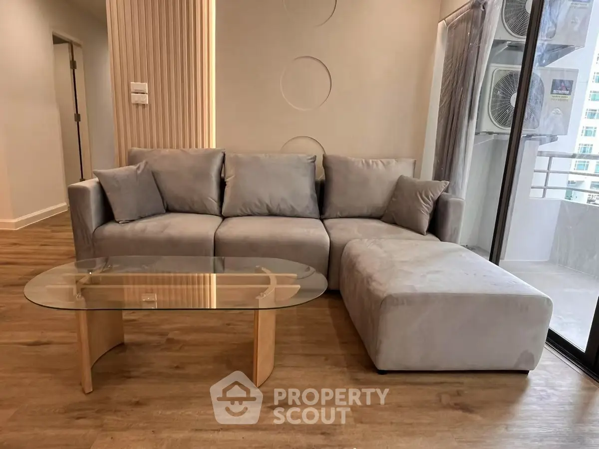 Modern living room with stylish gray sectional sofa and glass coffee table on wooden floor.