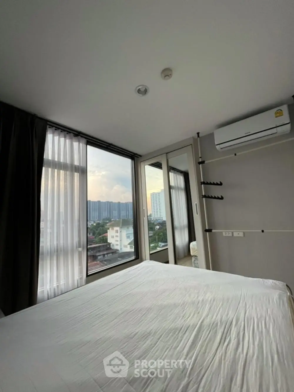 Modern bedroom with large windows offering city view and air conditioning unit.