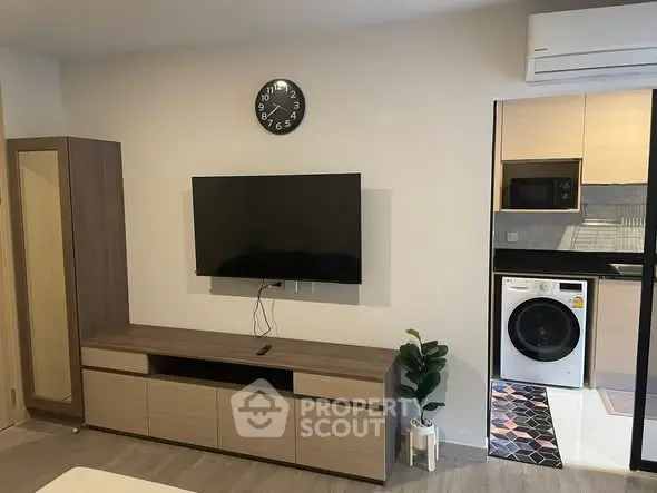 Modern living room with wall-mounted TV and adjacent kitchen featuring washing machine.
